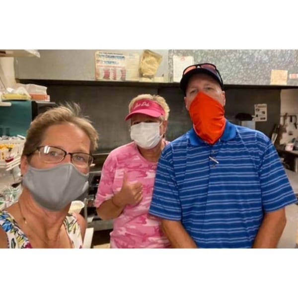 Three masked Lee's Deli employees, two women and one man, pose for a selfie in the kitchen.