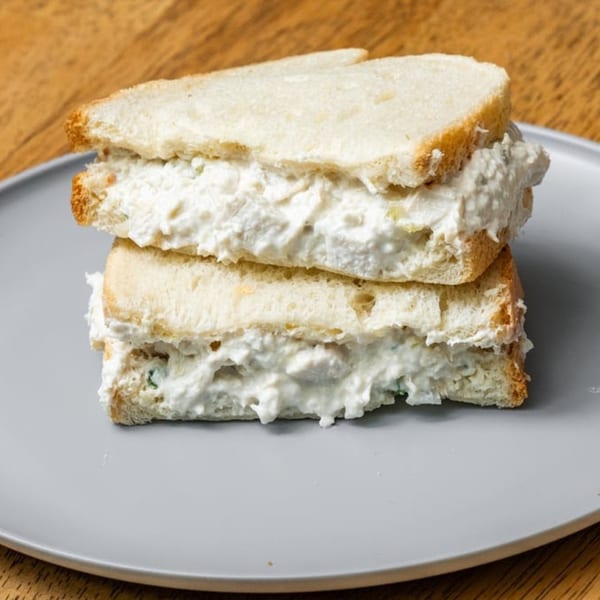 A stacked chicken salad sandwich on white bread, overflowing with creamy filling, on a gray plate.