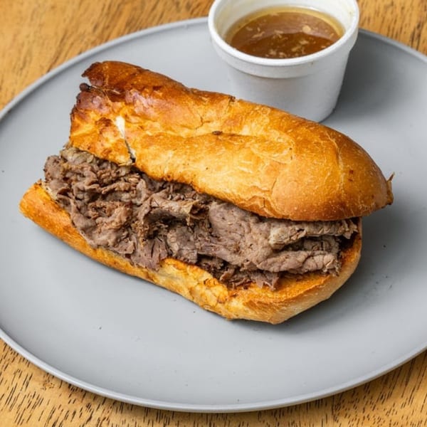 A Lee's Deli sub-sandwich with thinly sliced meat and a side of au jus on a gray plate.