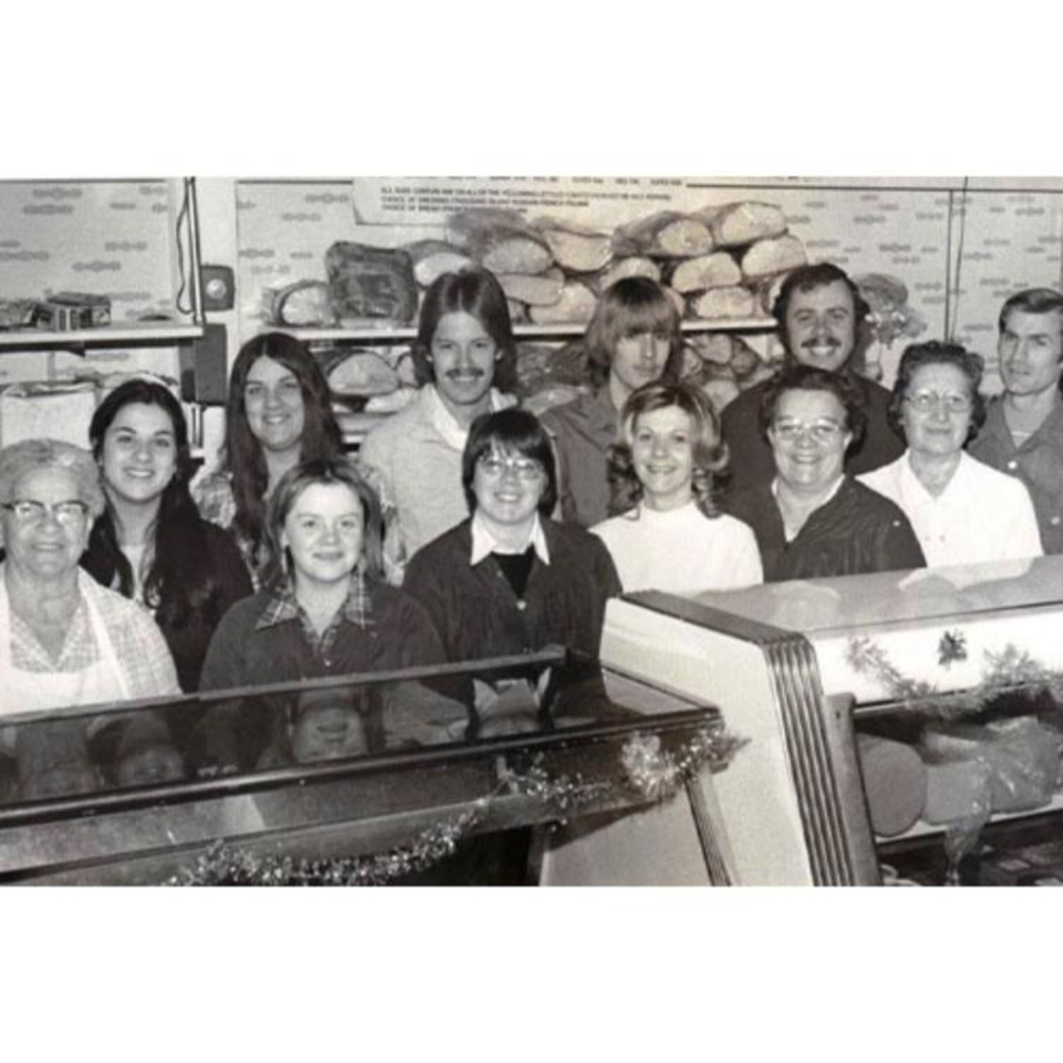 Black and white photo of a large group of Lee's Deli employees smiling behind a counter.