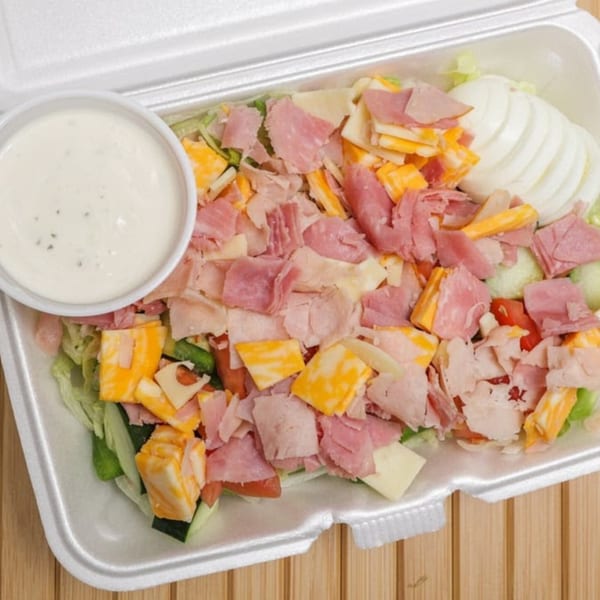 Lee's Deli chef salad with ham, cheese, onions, and dressing in a white takeout container.